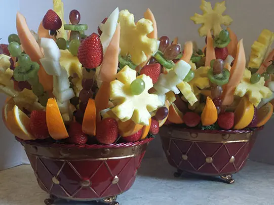Two fruit bouquets with pineapple flowers, grapes, and strawberries