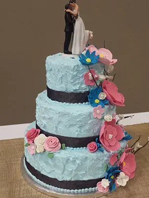 Four tiers with pink and teal flowers and a bride and groom topper