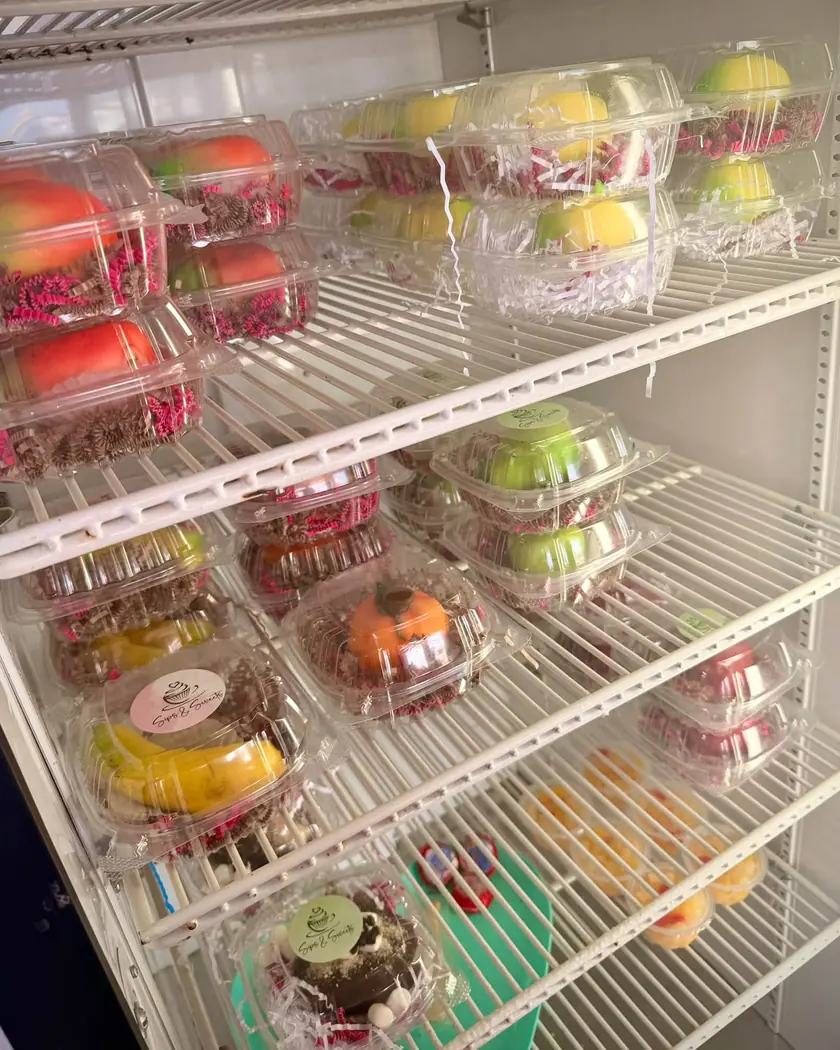 Shelves of fruit-shaped pastries in clear boxes: peaches, lemons, green apples, a pumpkin, and bananas