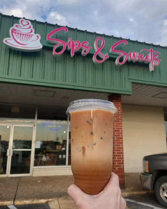 The Sips & Sweets storefront: a pink script sign on a green building, with an iced coffee held up in front