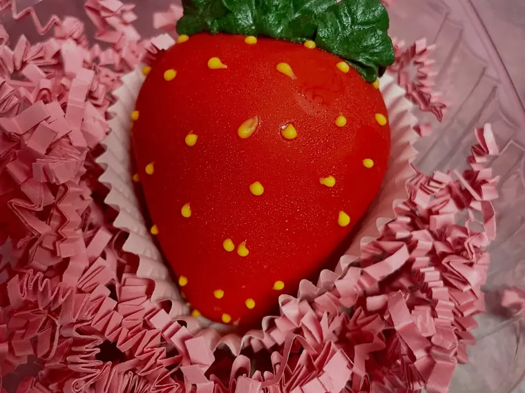 A glossy red pastry shaped like a strawberry, resting on pink paper