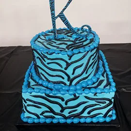 A two-tier blue zebra print cake with a glitter K topper